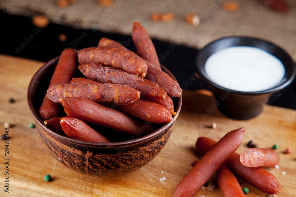 Wall mural Close up view on sausages. Tasty beer snack wurst salami. appetizing beer snack sekective focus. Table with salami sausage, white sauce and glass of beer. Dark background