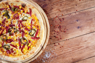 Top view hot chili pizza with corn, salami and red sauce on wooden background. Food flat lay. Copy space. Italian cuisine. Fresh homemade sliced pizza