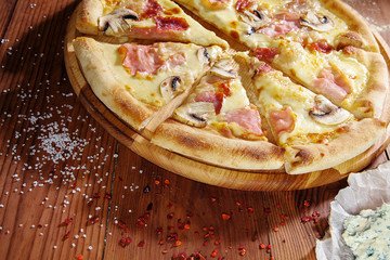Top view hot pizza ham, mozzarella, mushrooms and white sauce on wooden background. Food flat lay. Copy space. Italian cuisine. Fresh homemade sliced pizza