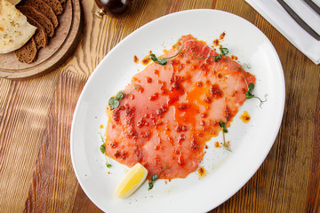 Top view on Salmon carpaccio with red caviar in white plate on wooden background. Flat lay food. Traditional Italian cusine seafood. Food photo for background. Copy space. Raw fish