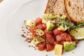Close up top view on beef tartare. Raw meat dish. Tartare with sauce, avocado, bread and lime in white plate. Delicious and tasty food on wooden background. Steak tartare