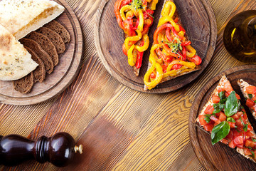 Top view on bruschetta with red, yellow baked, roasted bell pepper and tomato with olive oil on wooden cutting board on wooden background. italian cuisine. Copy space. Two tasty bruschetta. food
