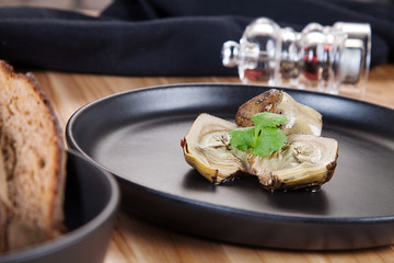 Close up view on boiled artichoke with bread on dark plate. Healthy, delicious vegan food. Copy space. Food photo for menu or recipe