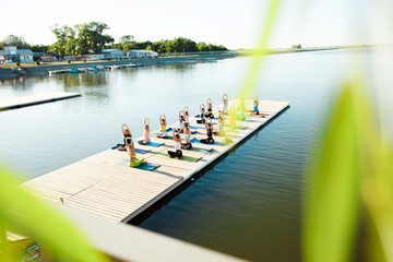 A big group of people attending yoga classes on a pontoon near the lake.