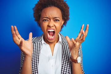 African american business executive woman over isolated blue background crazy and mad shouting and yelling with aggressive expression and arms raised. Frustration concept.