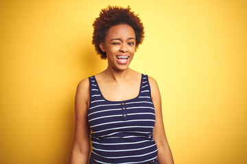 Beauitul african american woman wearing summer t-shirt over isolated yellow background winking looking at the camera with sexy expression, cheerful and happy face.