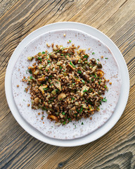 buckwheat porridge on handmade plate with  wild mushrooms, onion, and salted cucumber decorated with dill and parsley