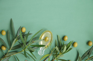 Flat lay olive oil in a glass in the form of olives and olive branch with green olives on a green...