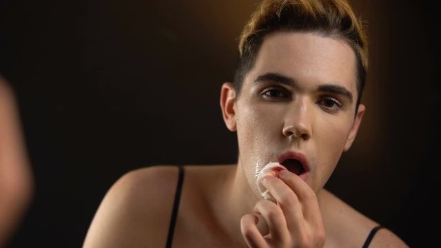 Crying transgender man removing makeup, feeling shame about queer identity