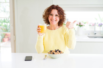 Senior woman eating healthy breakfast in the morning at home very happy pointing with hand and finger to the side