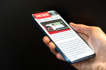 Fototapeta na wymiar A man holding mobile smart phone with news on screen. Newspaper online portal in browser.