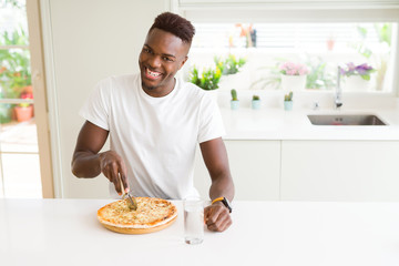 African american man eating cheese pizza at home with a happy face standing and smiling with a confident smile showing teeth