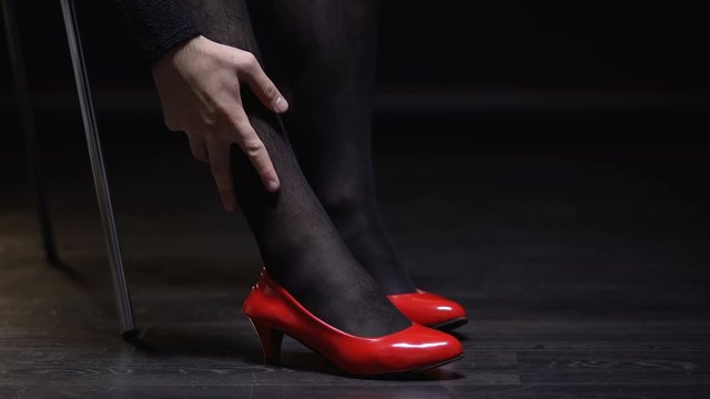 Transgender man in female shoes and pantyhose stroking leg, admiring femininity