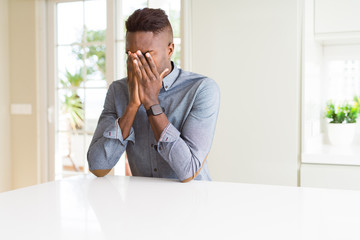 Fototapeta na wymiar Handsome african american man on white table with sad expression covering face with hands while crying. Depression concept.