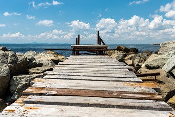 An old, wooden jetty over the beautiful Black Sea in Bulgaria, standing on a stony shore, in the background a sky with clouds.
