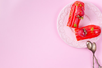 Traditional French dessert. Eclair with strawberries with two vintage spoons. Pink background. Copy space