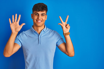 Young indian man wearing casual polo standing over isolated blue background showing and pointing up with fingers number eight while smiling confident and happy.