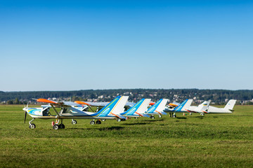 Small and light airplanes stand on a lawn of field airfield waiting for a departure in summer sunny day.