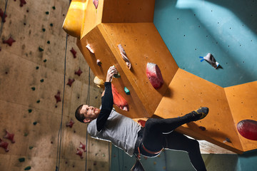 Fototapeta na wymiar Side view of athletic strong student with physical disability training hard at indoor bouldering sport center, enjoys his extreme hobby that helps to release stress and bad mood.