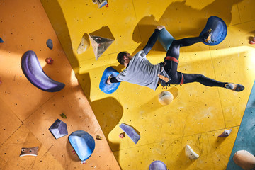 Back view of young strong rock climber without forearm training at yellow climbing wall with...