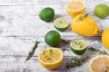 Lemons and limes with rosemary and thyme. Whole citrus fruits and halves on white wooden table