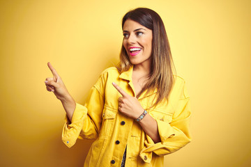 Young beautiful woman wearing denim jacket standing over yellow isolated background smiling and looking at the camera pointing with two hands and fingers to the side.