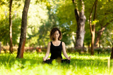 Naklejka na ściany i meble Attractive and peaceful woman sitting in yoga lotus position in the morning in park. Meditation, concentration and relaxation.