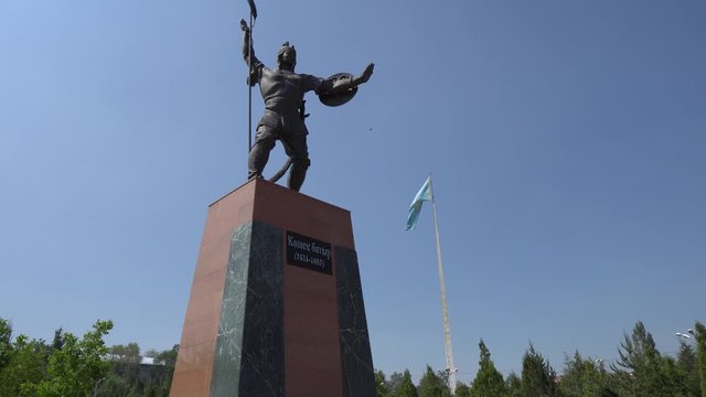  Taraz Presidential Park Statue of Koshek Batyr Holding a Spear with Huge Waving Kazakhstan Flag at Background on a Sunny Blue Sky Day