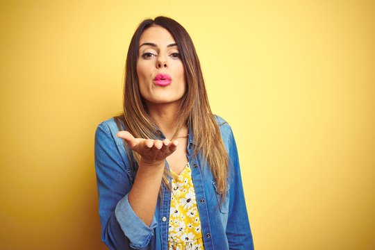 Young beautiful woman standing over yellow isolated background looking at the camera blowing a kiss with hand on air being lovely and sexy. Love expression.