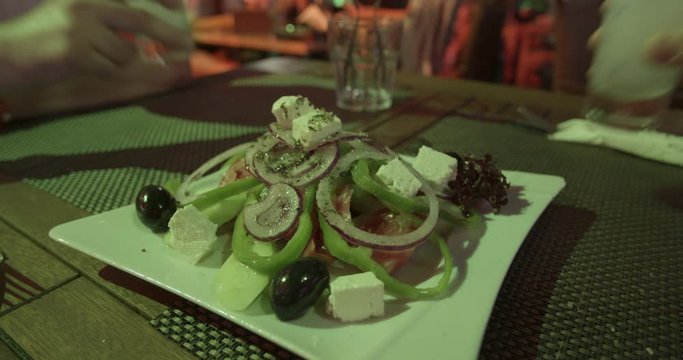 Greek salad close-up and ouzo toast in background in a restaurant at night