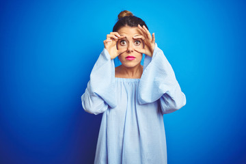 Young beautiful woman wearing bun hairstyle over blue isolated background Trying to open eyes with fingers, sleepy and tired for morning fatigue