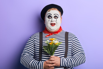 surprised excited clown holding flowers in hands isolated on white, going to give them to a lover....