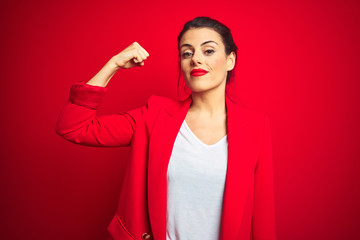 Young beautiful business woman standing over red isolated background Strong person showing arm...