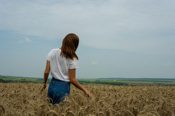 a young girl in a white t-shirt stands in a field of wheat and yellow ears to her waist