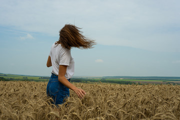a young girl in a white t-shirt stands in a field of wheat and yellow ears to her waist