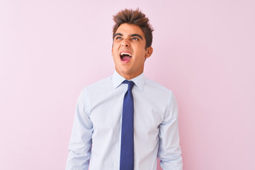 Young handsome businessman wearing shirt and tie standing over isolated pink background angry and mad screaming frustrated and furious, shouting with anger. Rage and aggressive concept.