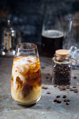 Ice coffee cold summer drink in a tall glass with pouring cream and coffee beans on a stone...