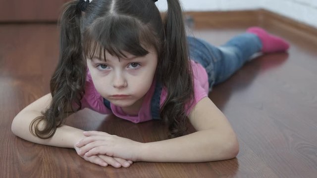 A sad child is lying on the floor. The offended little girl lies face down on the floor.