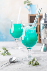 Colorful summer cocktail Blue Hawaii or iced blue lagoon alcohol drink with mint on light stone background