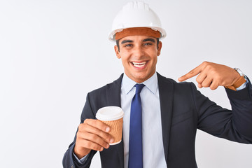Young handsome architect man wearing helmet drinking coffee over isolated white background with surprise face pointing finger to himself