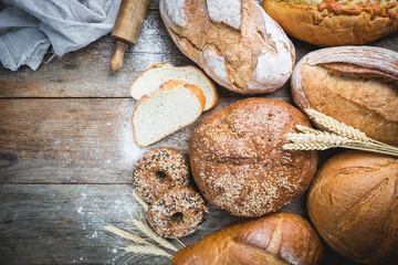 Assortment of fresh baked bread and buns on wooden table background, top view