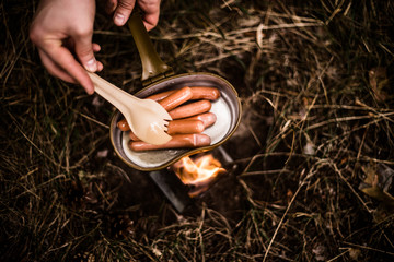 Sausages are fried over an open fire in a pan