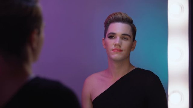 Genderqueer with half-face makeup looking in mirror, non-binary identity concept