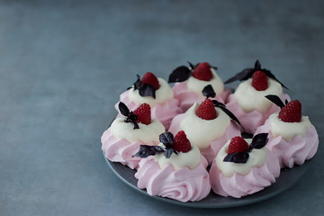 Raspberry meringues with fresh raspberries, basil and whipped cream on a gray plate.