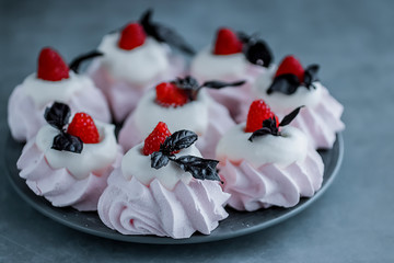 Raspberry meringues with fresh raspberries, basil and whipped cream on a gray plate.