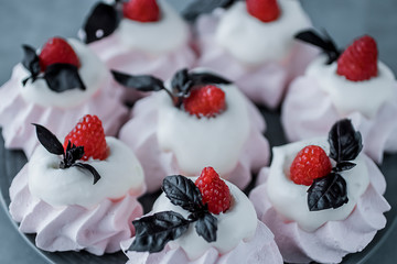 Raspberry meringues with fresh raspberries, basil and whipped cream on a gray plate.
