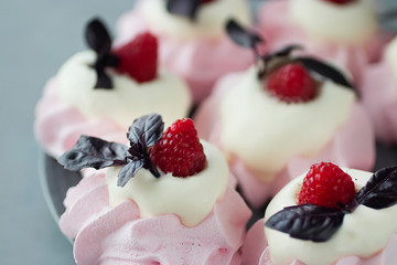 Raspberry meringues with fresh raspberries, basil and whipped cream on a gray plate.