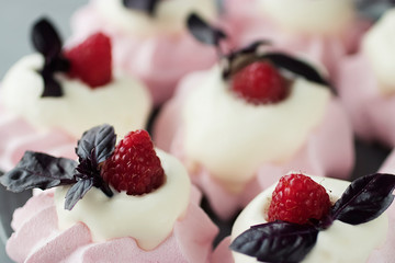 Raspberry meringues with fresh raspberries, basil and whipped cream on a gray plate.