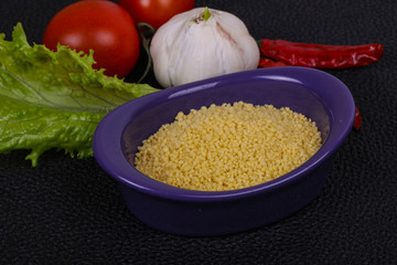 Raw couscous in the bowl served salad leaves, tomato and pepper
