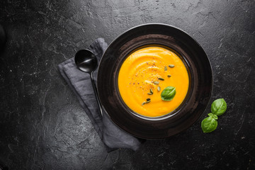 Vegetarian autumn pumpkin cream soup with seeds on dark background, top view